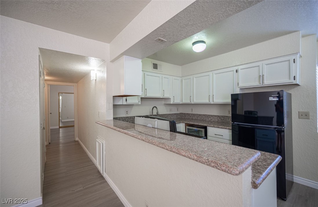 5336 Mancos Court, Unit 2 Las Vegas, NV 89119 - Photo 17 of 31 Kitchen featuring white cabinets, a peninsula, freestanding refrigerator, dark stone counters, and a textured wall