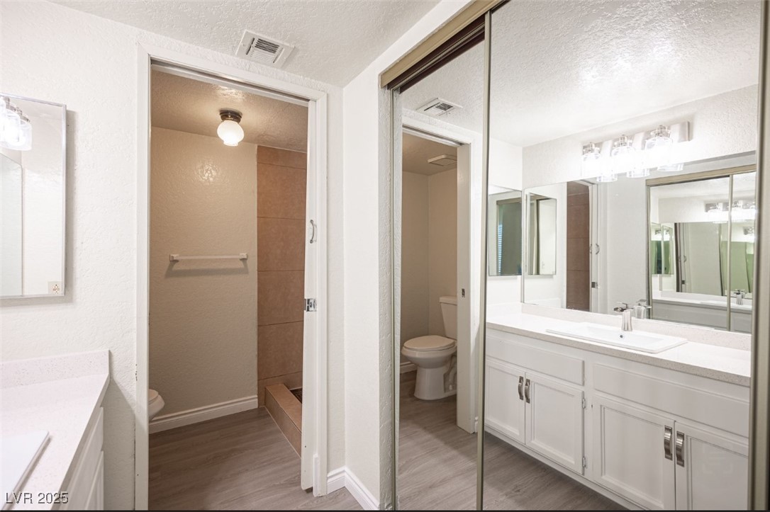 5336 Mancos Court, Unit 2 Las Vegas, NV 89119 - Photo 22 of 31 Full bathroom with two vanities, a textured ceiling, dark wood finished floors, and a stall shower