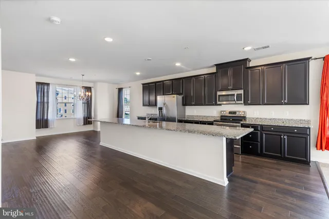 a kitchen with stainless steel appliances granite countertop wooden cabinets a refrigerator a stove a sink and a oven with wooden floors