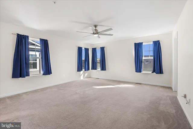a view of an empty room with chandelier fan and windows