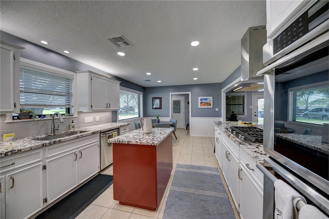 1600 Pecan Street Brenham, TX 77833 - Photo 22 of 33 Kitchen with stainless steel appliances, granite counter tops, sink, a center island, a textured ceiling, and decorative backsplash
