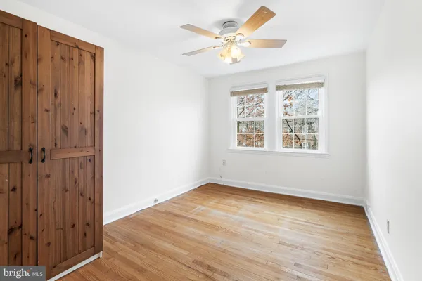 an empty room with wooden floor ceiling fan and windows