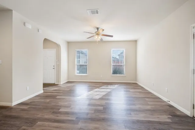 an empty room with wooden floor chandelier fan and windows