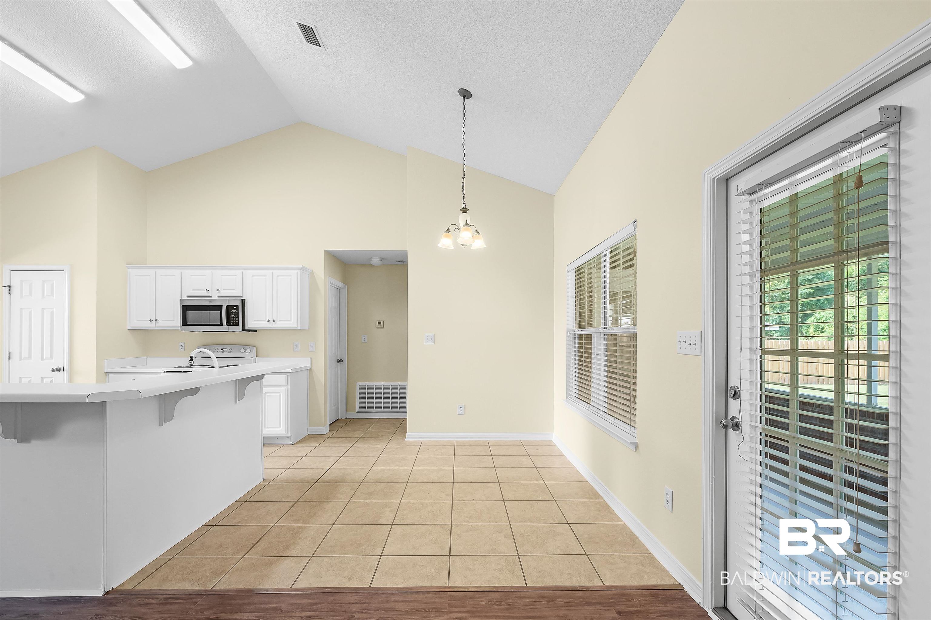 12443 Venice Boulevard Foley, AL 36535 - Photo 28 of 59 Kitchen with light tile patterned floors, decorative light fixtures, a kitchen breakfast bar, lofted ceiling, and white cabinets