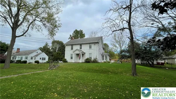 a view of a white house with a big yard and large trees