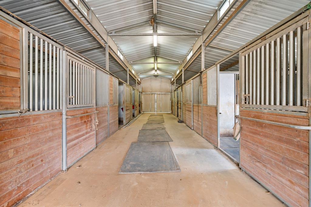 7260 Hudson Cemetery Road Mansfield, TX 76063 - Photo 5 of 40 Barn interior with concrete flooring and multiple stalls featuring horizontal wood paneling and metal bar upper sections