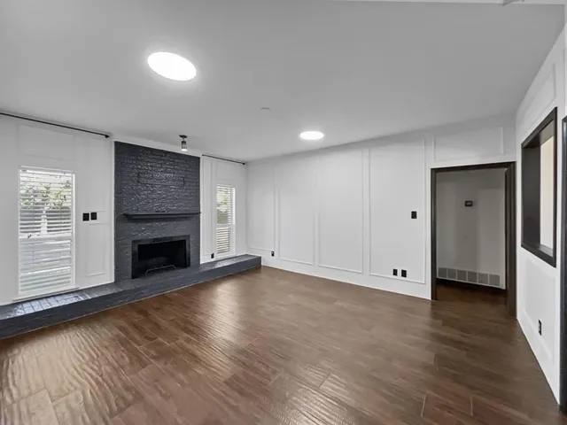 a view of an empty room with wooden floor fireplace and a window