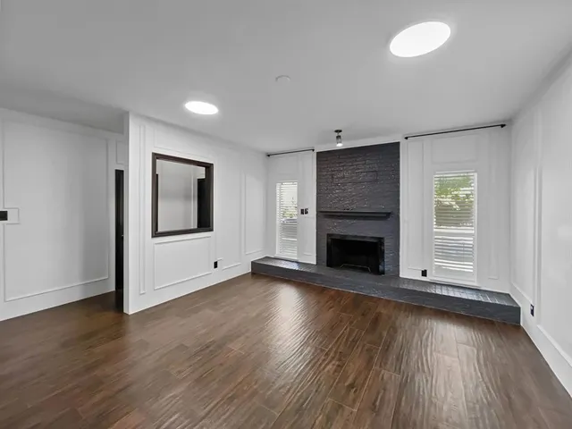 an empty room with wooden floor fireplace and windows