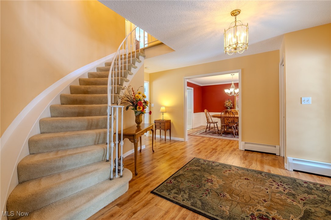 535 Barrington Ridge Road Painesville, OH 44077 - Photo 14 of 48 Foyer featuring baseboard heating, hardwood / wood-style flooring, a textured ceiling, and a notable chandelier