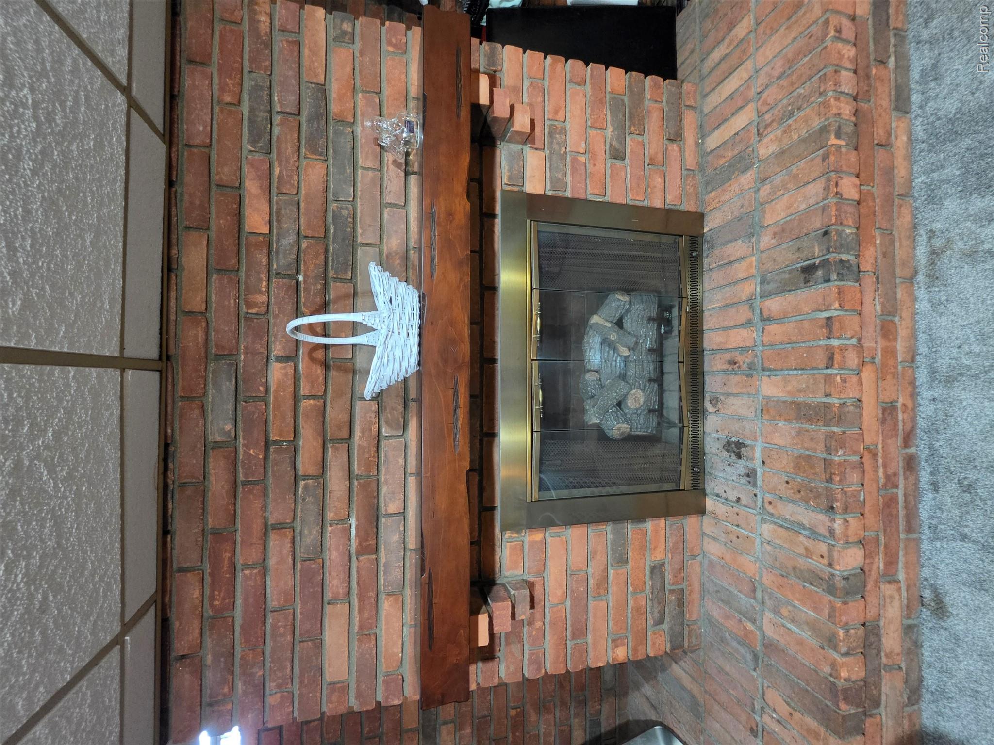 18503 Bittersweet Road Fraser, MI 48026 - Photo 23 of 34 Brick fireplace featuring a wood mantel, a stainless steel firebox enclosure with glass doors, and a brick hearth