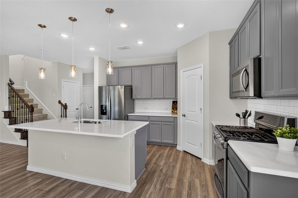 8715 Royal Star Road Rowlett, TX 75089 - Photo 19 of 39 Kitchen featuring a large island with sink, stainless steel appliances, abundant cabinetry, white subway tile backsplash, and wood-finish flooring