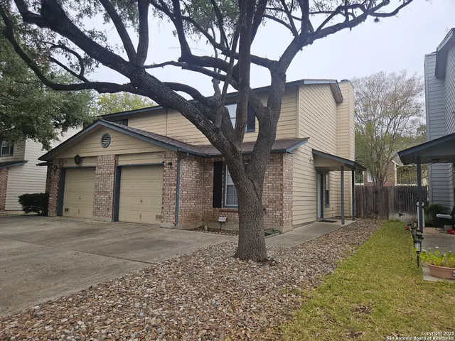 a front view of a house with a yard and large tree