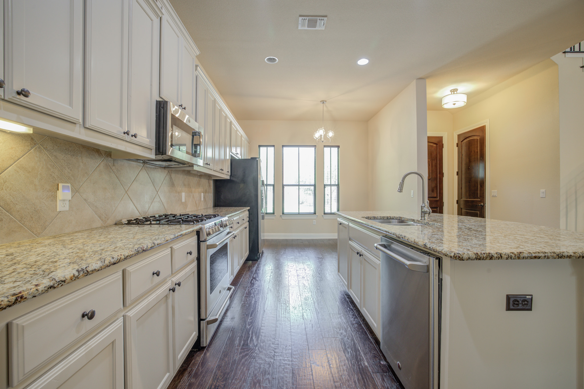 4524 Berkman Drive Austin, TX 78723 - Photo 13 of 38 Kitchen featuring granite countertops, extensive cabinetry, stainless steel appliances, a tiled backsplash, and wood-finish flooring