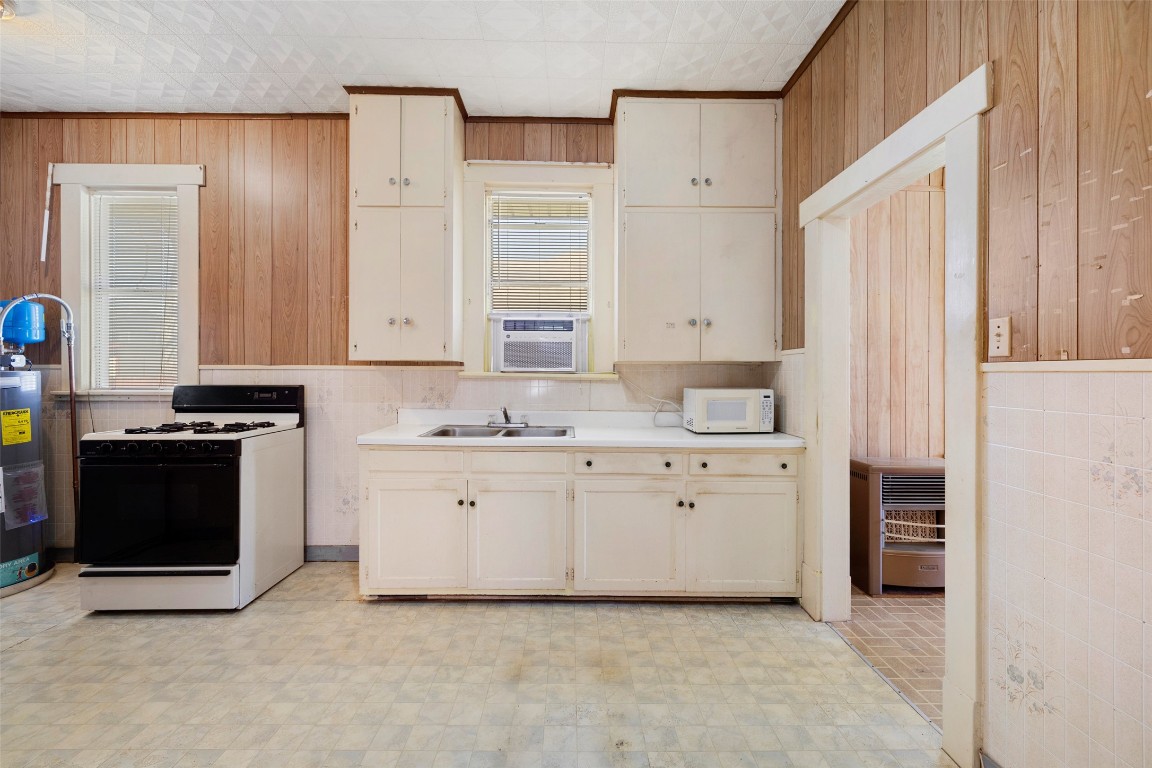 303 Vernon Street Taylor, TX 76574 - Photo 25 of 37 Kitchen with light countertops, white microwave, wood walls, a sink, and gas range