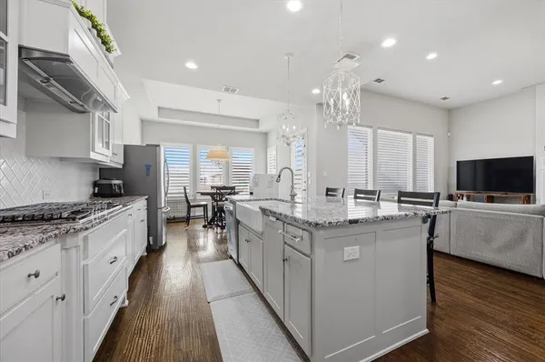 a kitchen with stainless steel appliances granite countertop a stove top oven a sink dishwasher and a refrigerator with wooden floor