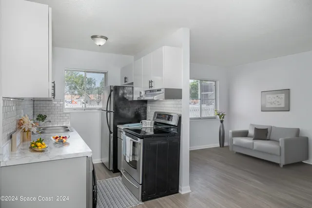 a kitchen with stainless steel appliances a stove a refrigerator a sink a stove and white cabinets with wooden floor