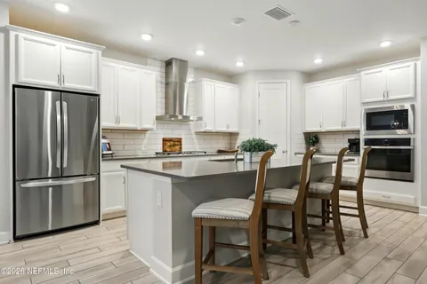 a kitchen with stainless steel appliances kitchen island granite countertop a stove a sink a refrigerator and white cabinets with wooden floor