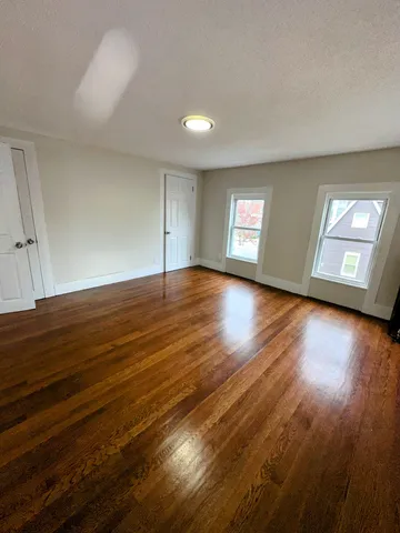 a view of an empty room with window and wooden floor