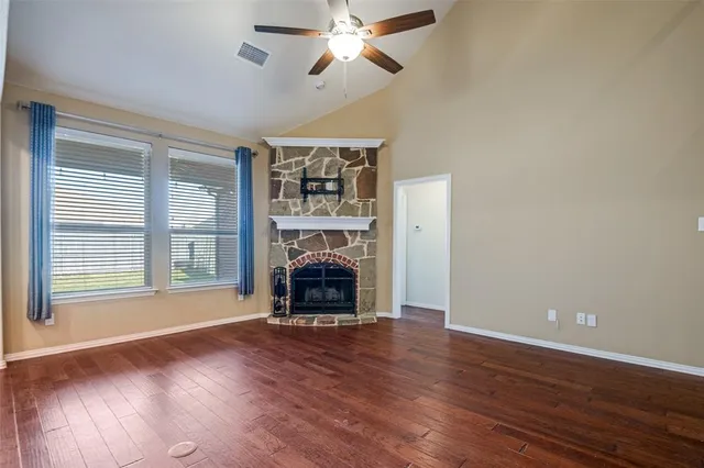 a view of an empty room with wooden floor fireplace and a window
