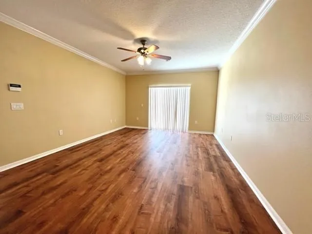 a view of an empty room with wooden floor and a ceiling fan