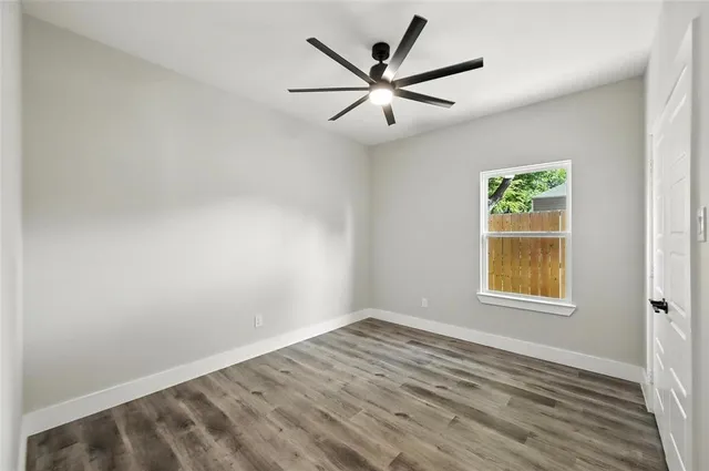 an empty room with wooden floor ceiling fan and windows