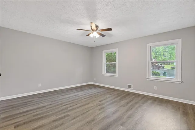 an empty room with wooden floor ceiling fan and windows