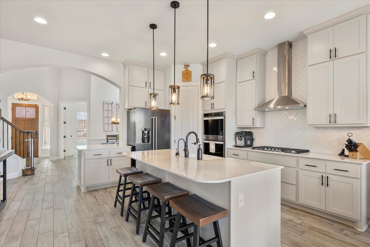 Kitchen featuring wall chimney range hood, arched walkways, decorative backsplash, light wood-style flooring, and appliances with stainless steel finishes