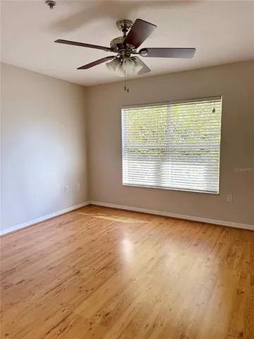 an empty room with wooden floor chandelier fan and windows