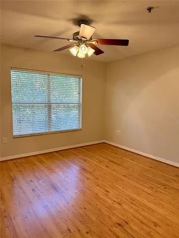 an empty room with wooden floor fan and windows