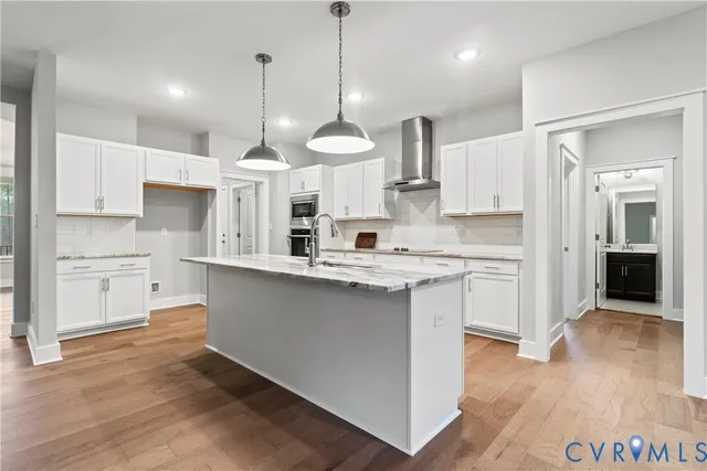 a kitchen with stainless steel appliances granite countertop a stove a sink dishwasher a refrigerator and white cabinets with wooden floor