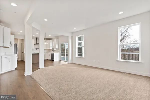 a view of an empty room with wooden floor and kitchen