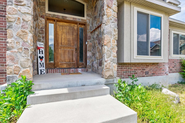 316 Azure Circle Draper, UT 84020 - Photo 9 of 48 Exterior featuring a natural wood entry door with side windows, stone column accents, and a complementary brick facade