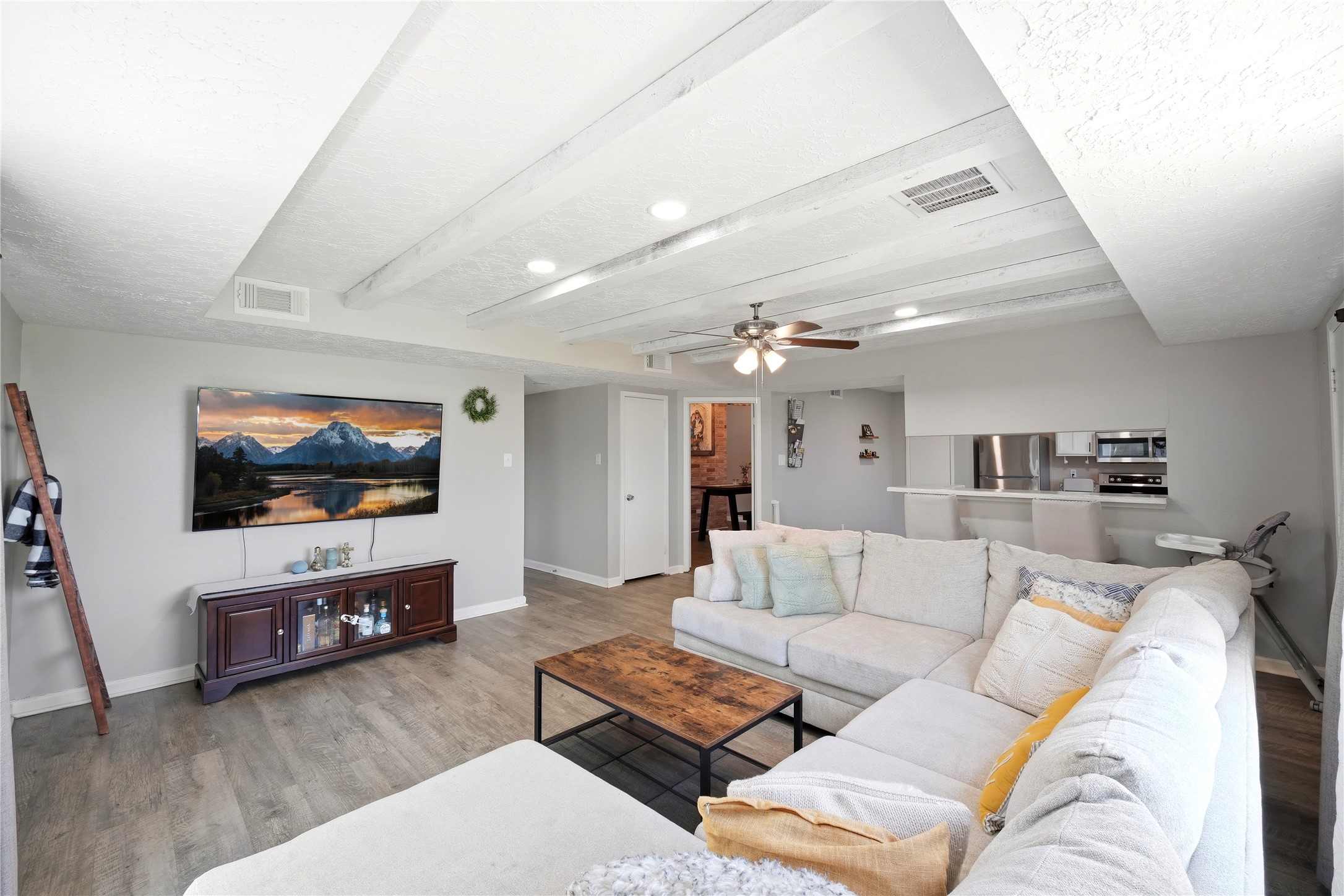4718 Temple Bell Drive Spring, TX 77388 - Photo 16 of 50 Spacious living room with a cozy sectional sofa, modern ceiling fan, and recessed lighting. Open layout connects to the kitchen. Features a wall-mounted TV and stylish wood floors.
