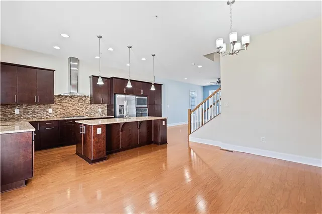 a kitchen with stainless steel appliances kitchen island granite countertop a refrigerator a sink dishwasher a stove and a dining table with wooden floor