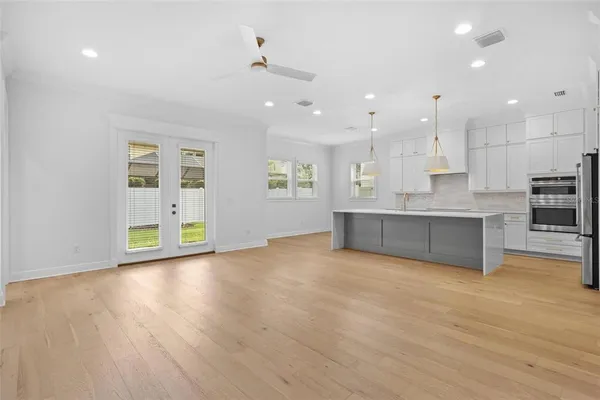a view of an empty room with kitchen and window