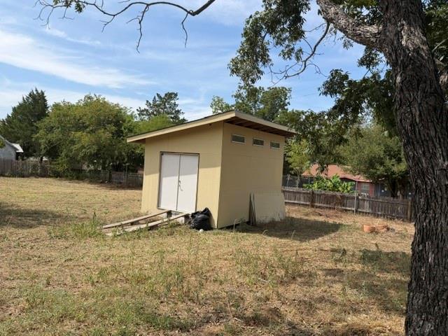 707 Madison Street Elgin, TX 78621 - Photo 3 of 4 A detached wooden storage shed sits on a spacious grass lawn bordered by mature trees.