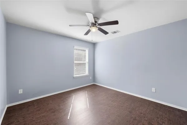 an empty room with wooden floor fan and windows