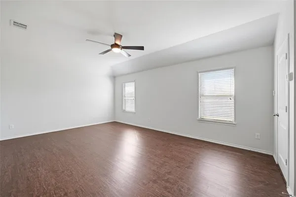 an empty room with wooden floor ceiling fan and windows