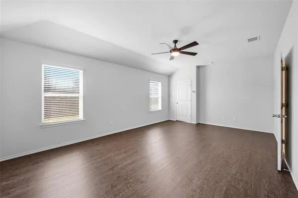 an empty room with wooden floor ceiling fan and windows