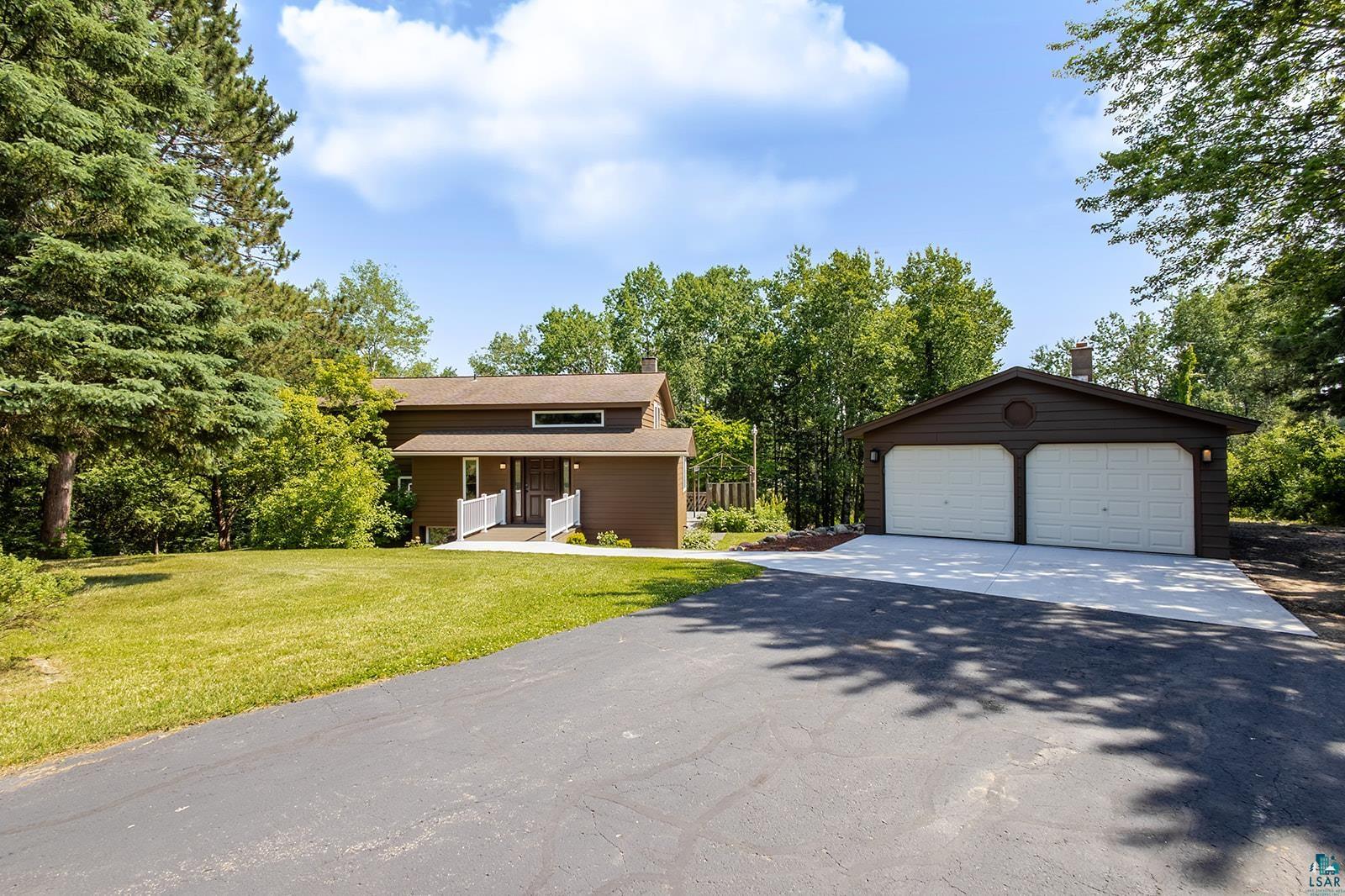 29 Ridge Road Esko, MN 55733 - Photo 1 of 41 Brown-sided residence featuring a covered front porch with white railing, set against a backdrop of mature trees and a manicured lawn