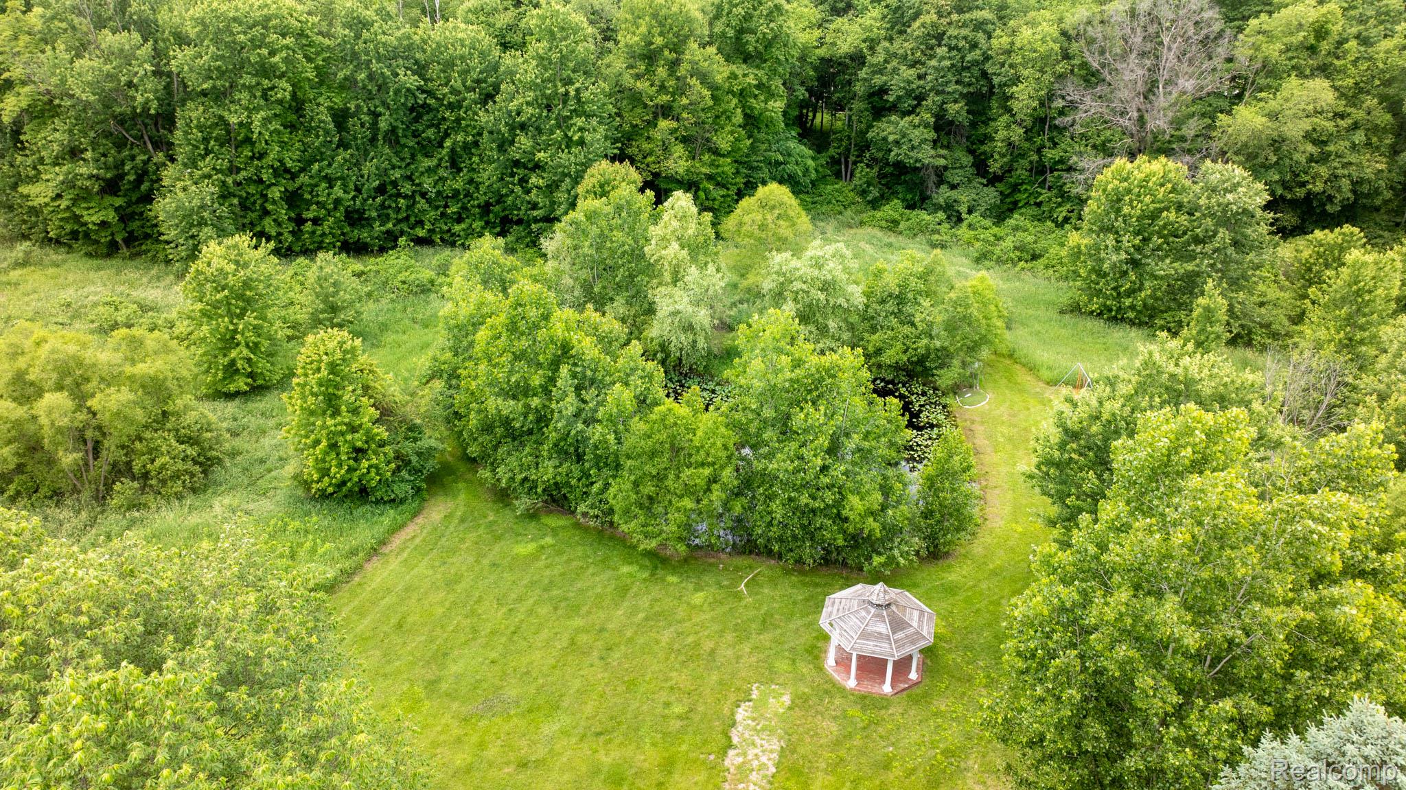 7333 Toma Road Dexter, MI 48130 - Photo 7 of 45 Spacious greenspace featuring a red-roofed gazebo, a stone path, and a circular water feature surrounded by mature trees