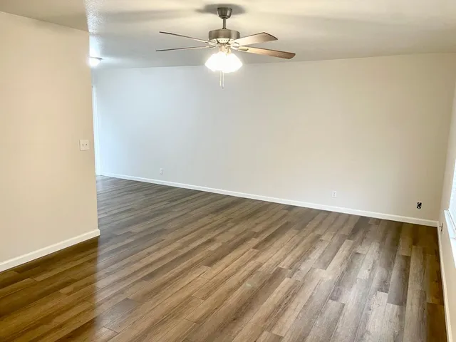 an empty room with wooden floor fan and window