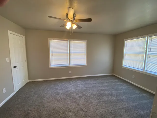 an empty room with chandelier fan and windows