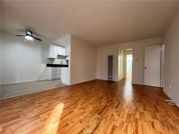 a view of empty room with wooden floor and kitchen