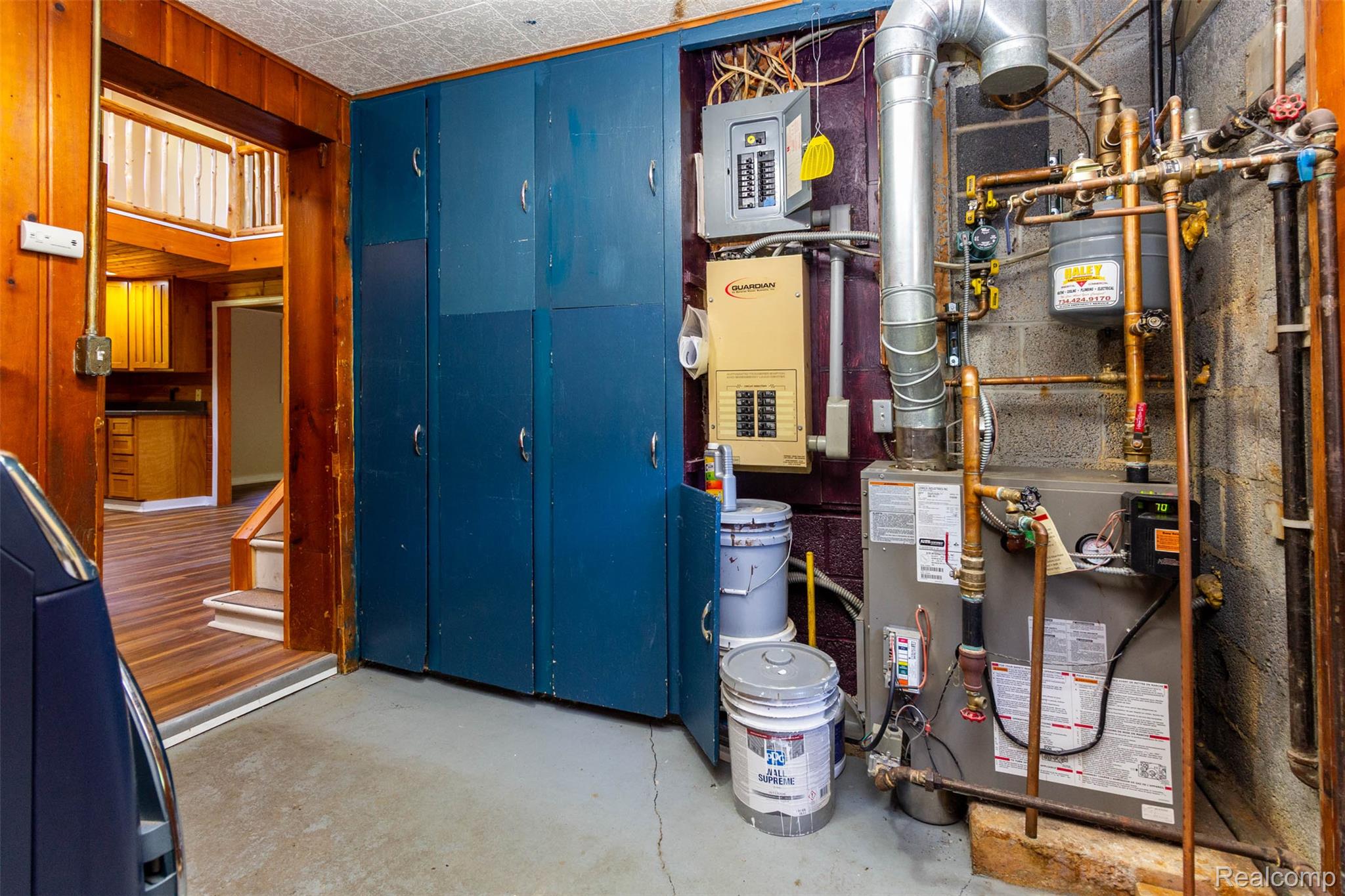 14044 Ridgemont Drive Gregory, MI 48137 - Photo 27 of 33 Utility area with exposed copper piping, water heater, and electrical panels, complemented by built-in blue cabinetry and concrete flooring