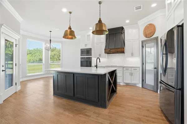 a kitchen with stainless steel appliances granite countertop a refrigerator a sink dishwasher a kitchen island a stove and a wooden floors