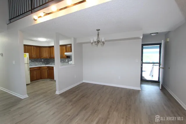 an empty room with wooden floor and kitchen view