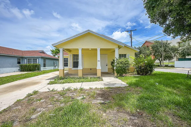 a view of yellow house with a big yard and potted plants