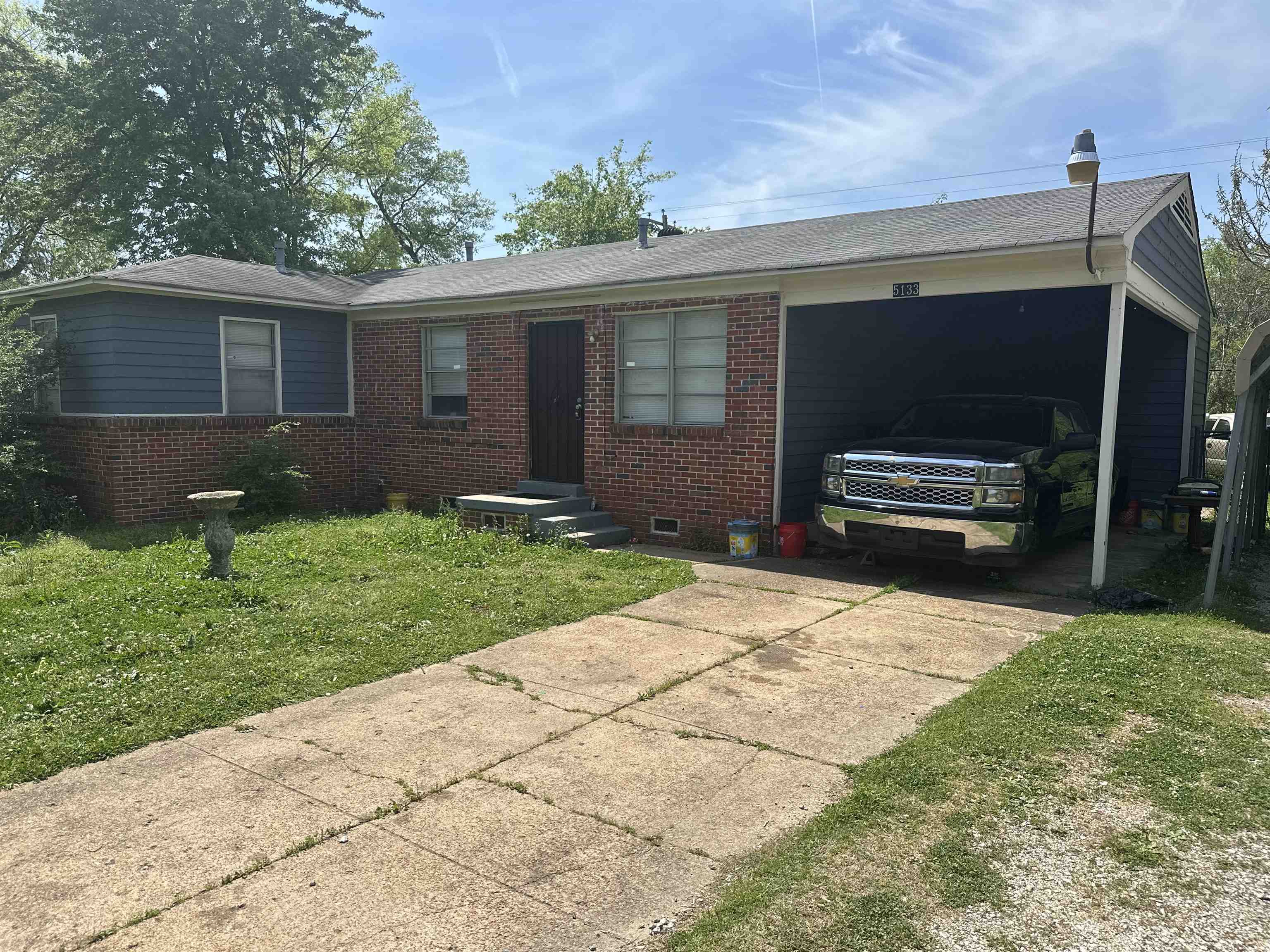 Ranch-style home featuring concrete driveway, brick siding, an attached carport, and a front lawn