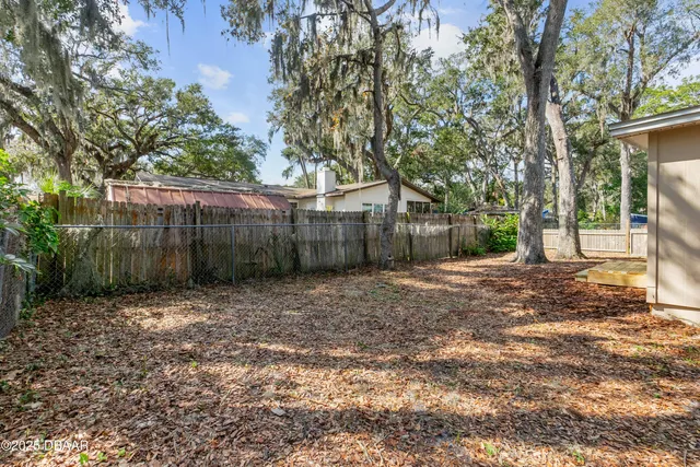 a view of a backyard with large trees and wooden fence